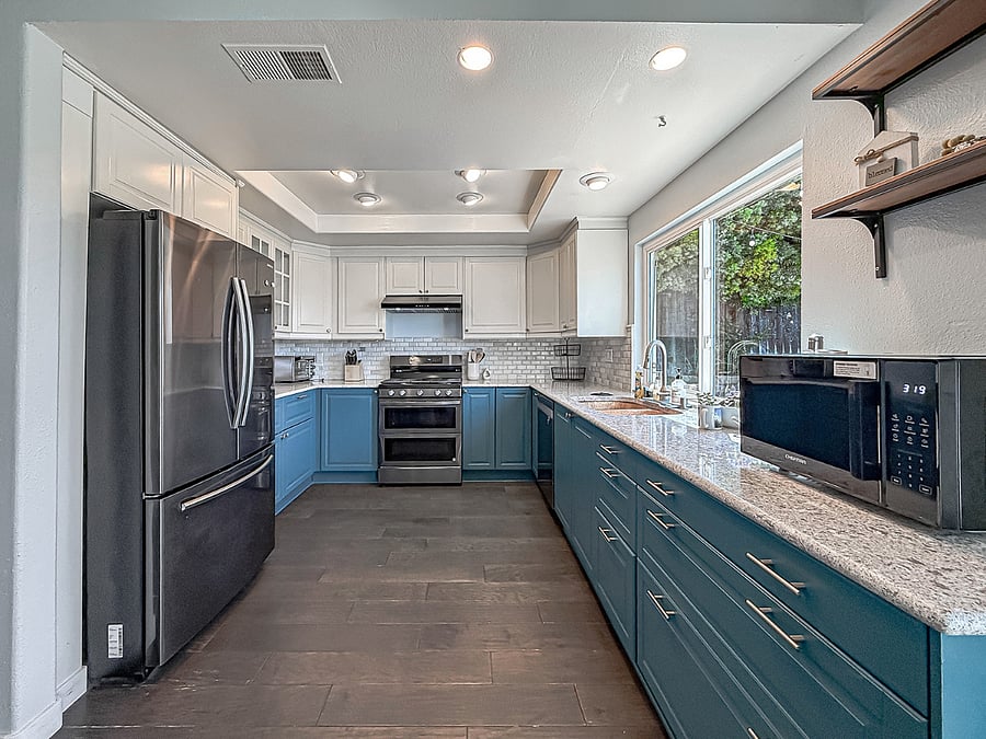 Interior - Bright furnished kitchen featuring stainless steel appliances, blue cabinetry, granite countertops, subway tile backsplash, and abundant natural light.