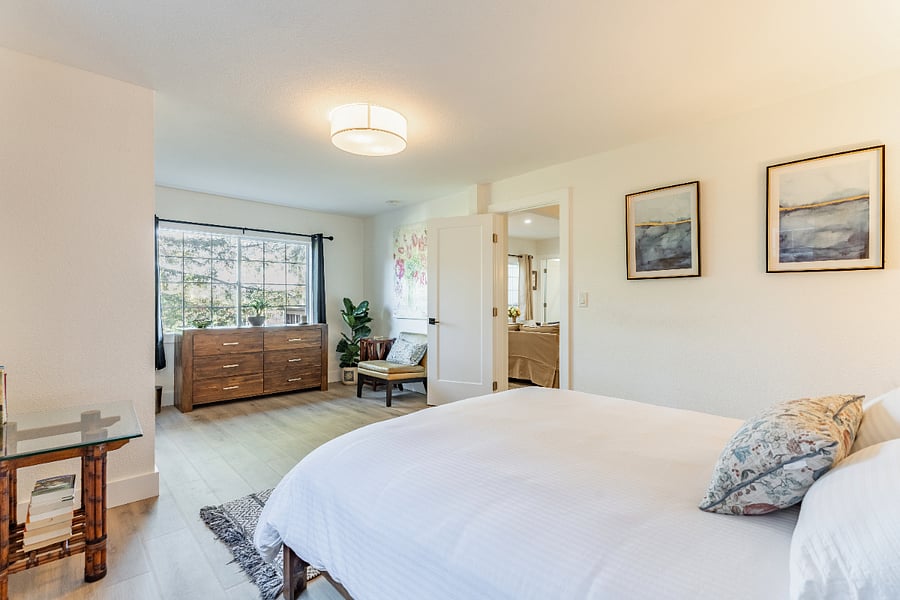 Spacious bedroom has large window with view of trees and nearby hills. There are blackout curtains on both windows.