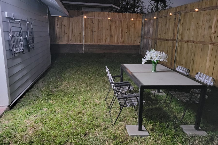 Backyard with table, chairs, umbrellas and accent lights.