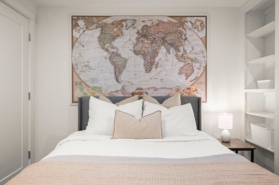 Bedroom with queen bed, bedside table, built-in shelving, and world-map accent wall.