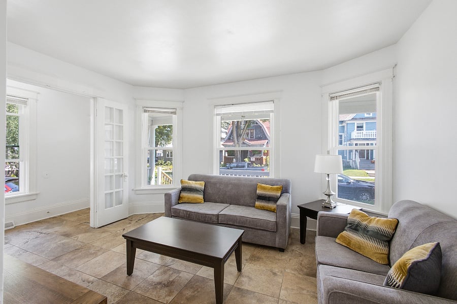 Living room with two gray sofas, yellow accent pillows, a dark wood coffee table, and tall windows facing the street