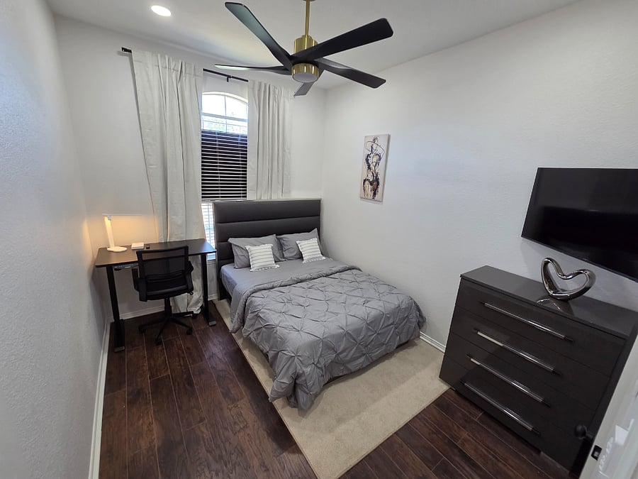 Hybrid bedroomworkspace featuring an ergonomic FlexiSpot chair, sitstand desk, 180 tilt smart TV, and open floor space for light exercise perfect for longterm stays and remote work.