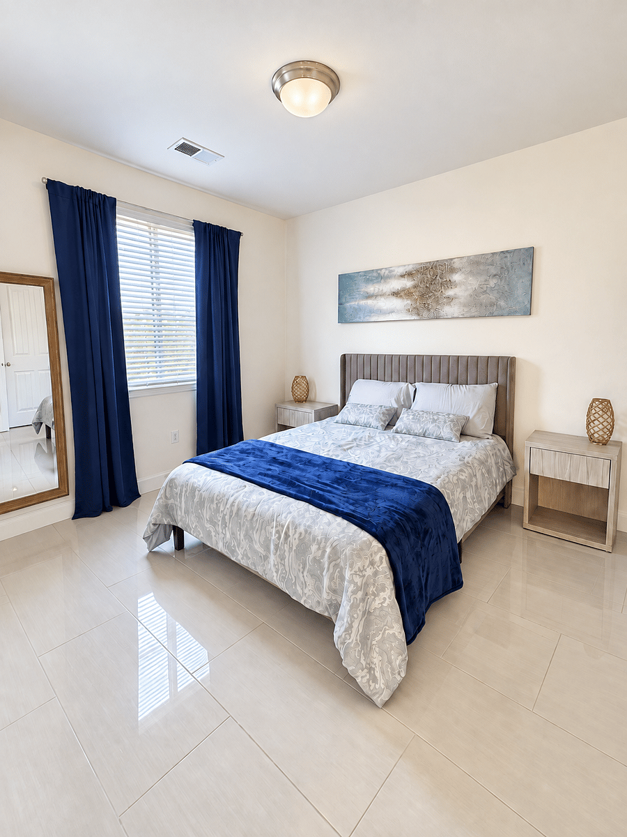 Bright, fully furnished private bedroom with a comfortable queen bed, nightstands, natural light, and blackout curtains for added privacy and restful sleep.