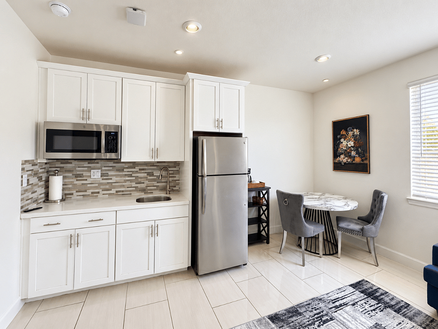 Bright kitchenette with full-size refrigerator, microwave oven, sink, ample cabinetry, and adjacent dining area.