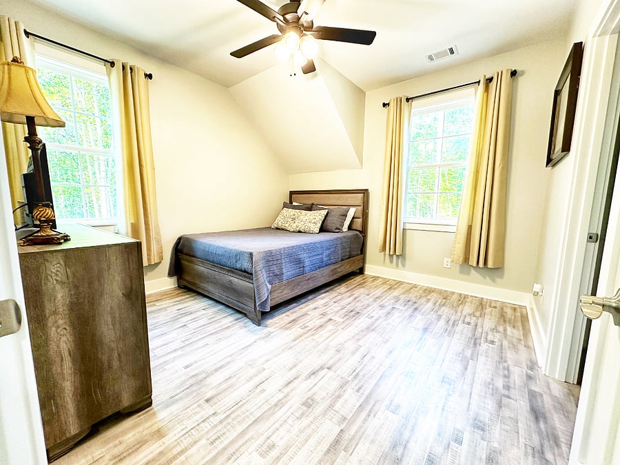 Comfortable primary bedroom with queen bed, dresser, TV, abundant natural light, and en suite bathroom.