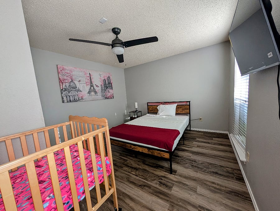 Fifth bedroom with a queen bed, ceiling fan, walk in closet, a crib and a 43" Smart TV.