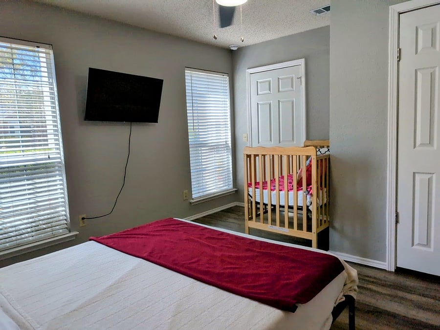 Fifth bedroom with a queen bed, ceiling fan, walk in closet, a crib and a 43" Smart TV.