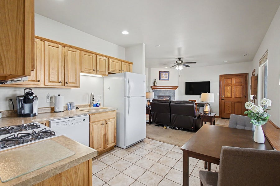 Open-concept kitchen and dining area flows seamlessly into the comfortable living room, complete with leather motion recliners, a gas fireplace, and a large Smart TV.