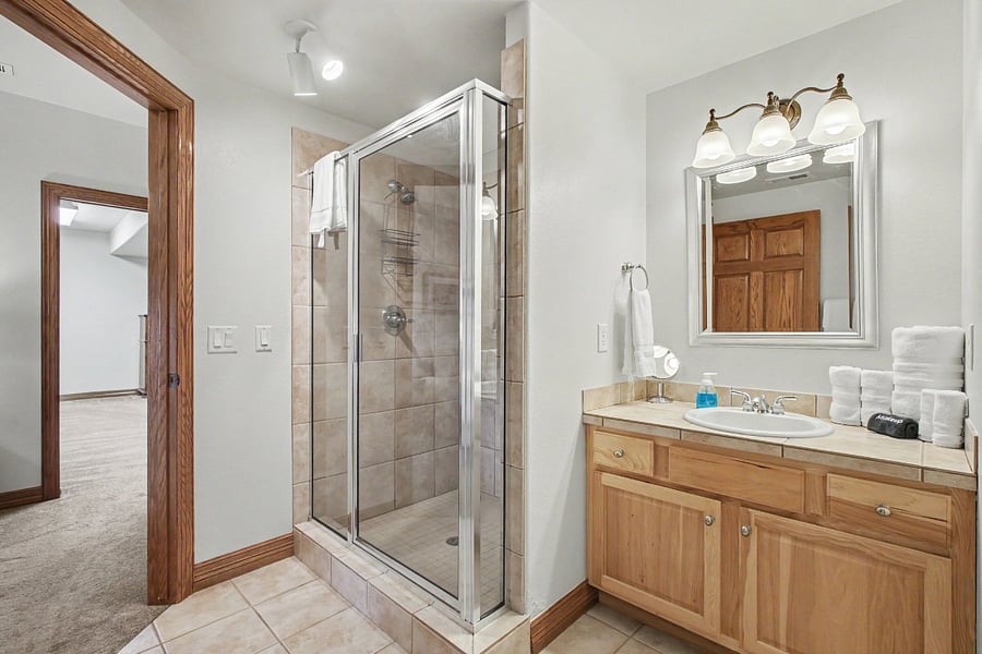 A separate bathing area features a tiled walk-in shower with a glass enclosure and a spacious second vanity, conveniently separated from the half bath by a privacy door