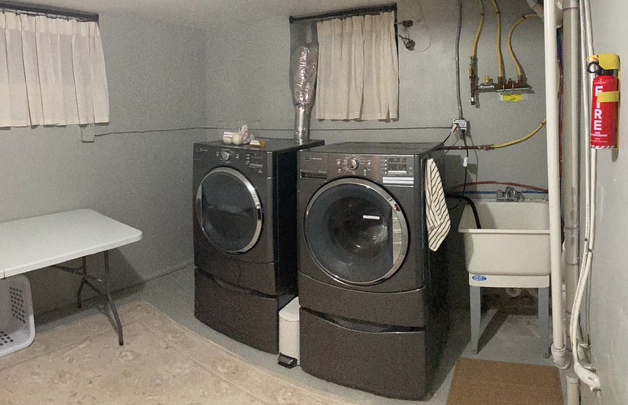 The private laundry area includes a full-size washer and dryer, utility sink, folding space, drying rack, and laundry essentials for convenient extended stays.