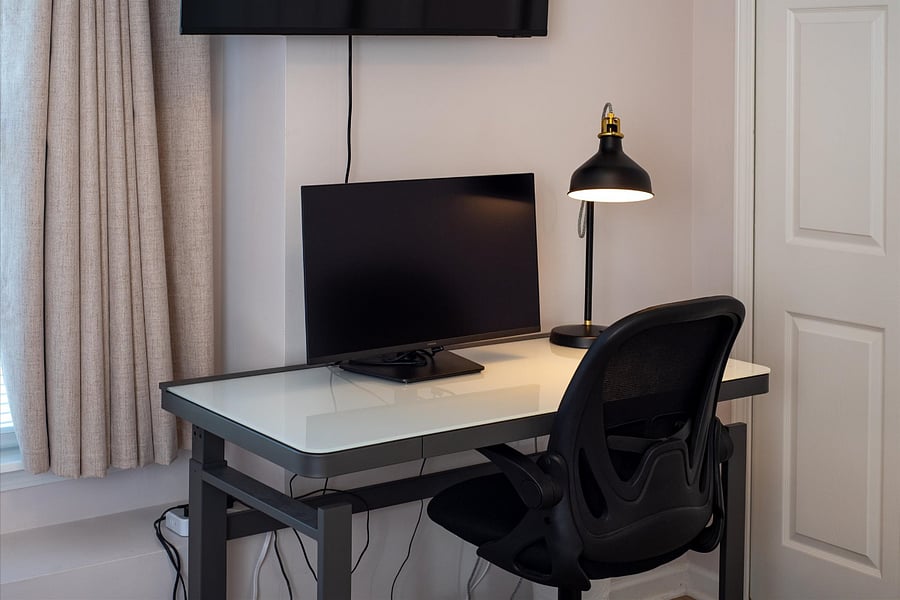 Electric standing desk with built in lighting, a large monitor, fast Wifi and a Smart TV in primary bedroom