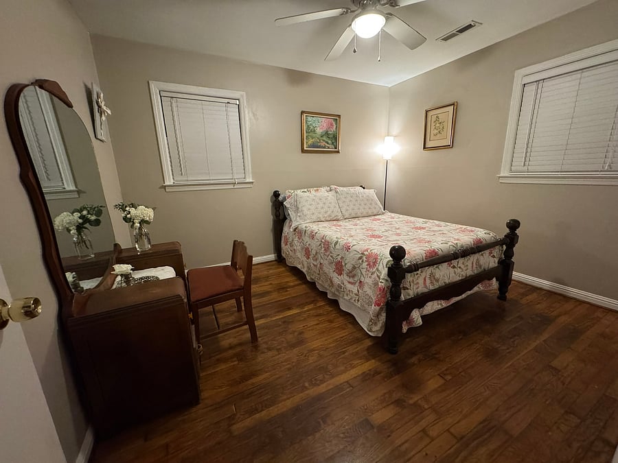 The second bedroom is quiet and relaxing, with freshly painted khaki walls and a midcentury vanity with curved mirror. Has two windows and a closet in the corner.