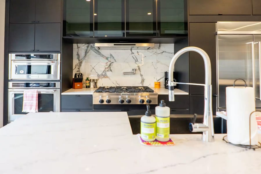 Four bar stools line the long island facing stainless appliances and black cabinets.