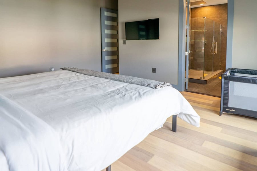 An open door reveals the dark-tile walk-in shower just off the bedroom.