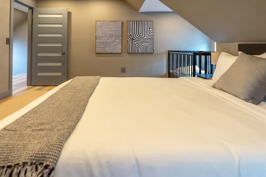 This attic bedroom offers a large bed, upholstered bench, and wooden crib.