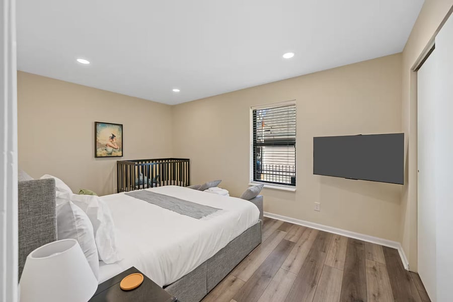 This family-friendly bedroom includes a grey upholstered bed and a crib.