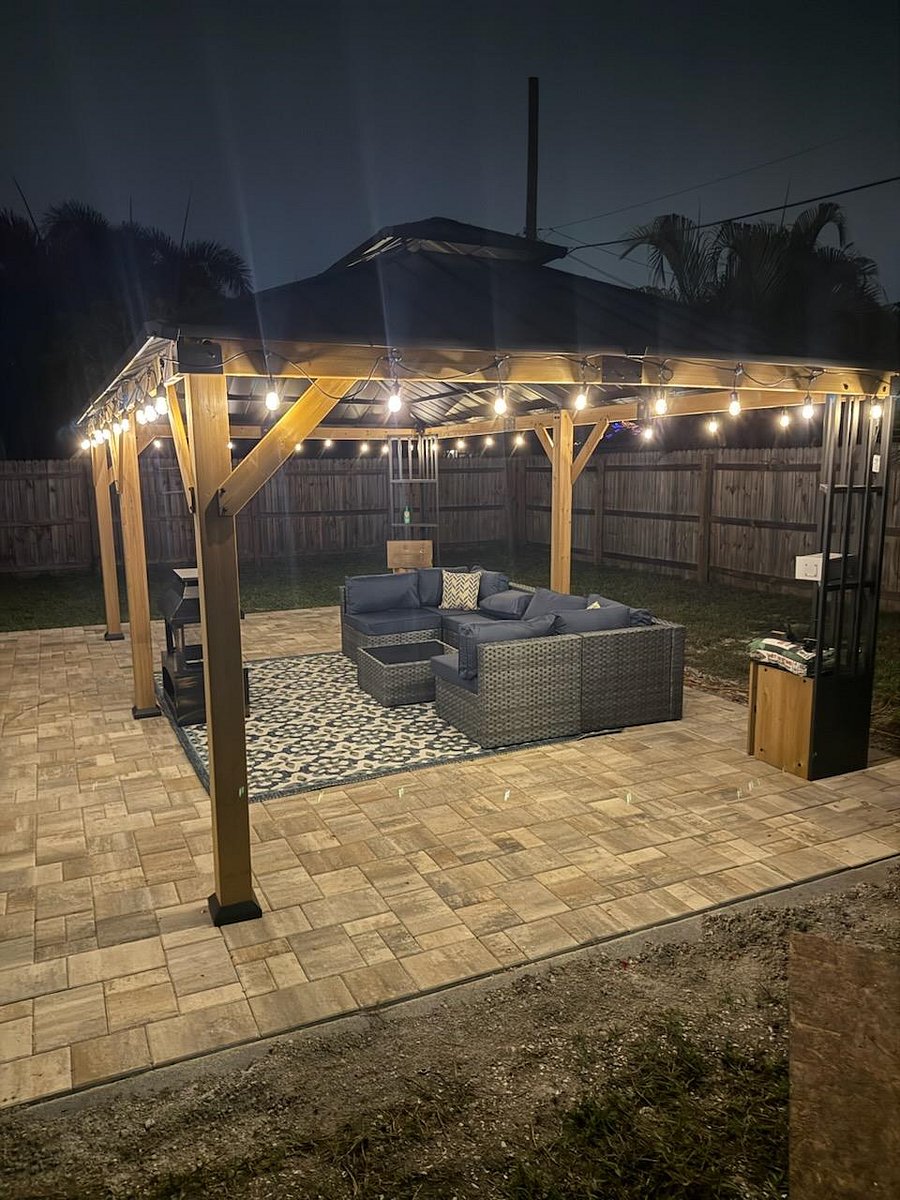 Spacious 16'x24' rear paver patio with new sectional couch, area rug, gazebo and firepit. Festive lighting is also present.
