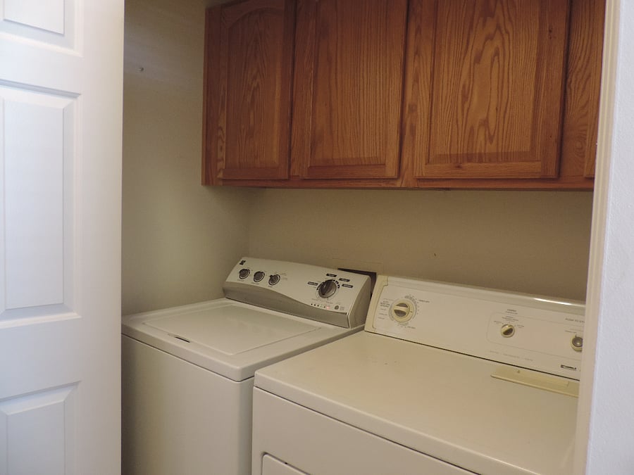 Indoor laundry machines with storage above, an iron, ironing board, and vacuum cleaner.