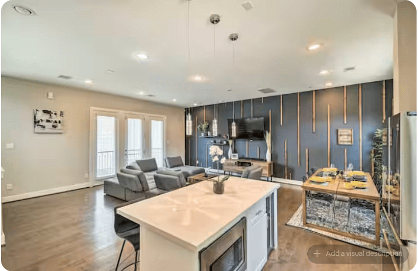 Bright open-concept kitchen, dining & living space with warm wood floors.
Island seating and a set dining table provide plenty of gathering space.
Comfortable lounge seating faces a striking accent wall and TV, with doors adding natural light.