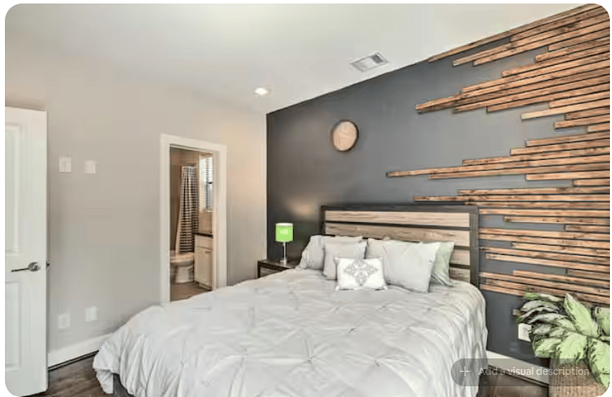 Stylish bedroom with a comfortable bed, warm wood floors & dramatic dark accent wall.
Natural wood detailing creates a distinctive focal point behind the bed.
Soft lighting, modern dcor & nearby bathroom access complete the space.