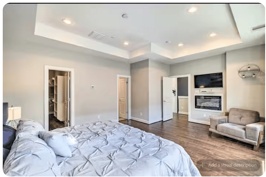Spacious bedroom with warm wood floors, tray ceiling & recessed lighting.
Wall-mounted TV and fireplace create a comfortable retreat, while a cozy sitting chair, walk-in closet & direct bathroom access add convenience.