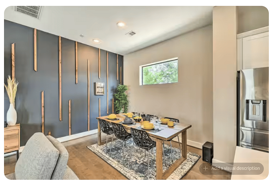 Stylish dining area with a set table, seating for six & patterned area rug.
A dramatic dark accent wall with natural wood detailing adds character, while a wide window brings in natural light beside the open kitchen.
