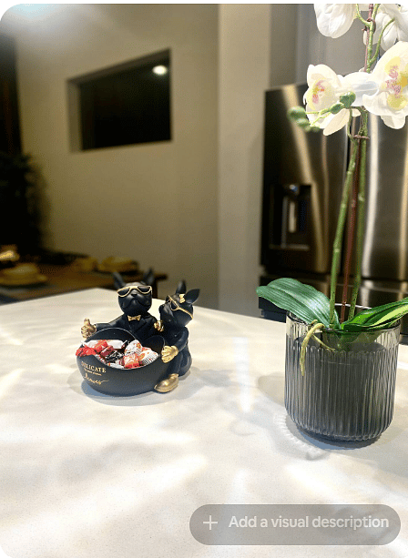 Thoughtful kitchen details add a welcoming touch, with complimentary treats displayed beside a decorative orchid.
The bright countertop, stainless steel refrigerator & nearby dining area highlight the homes polished, guest-ready feel.