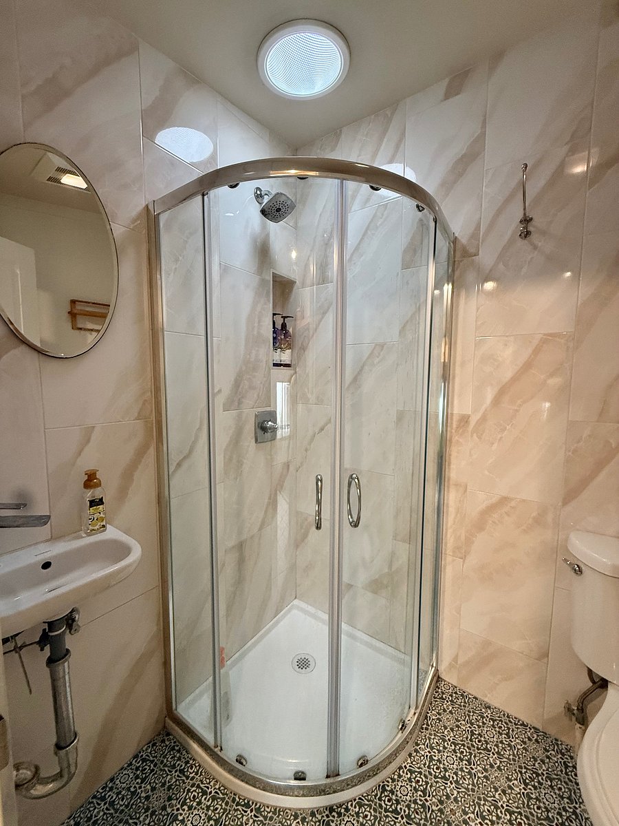Bathroom-single stall shower, small sink, toilet and shelving