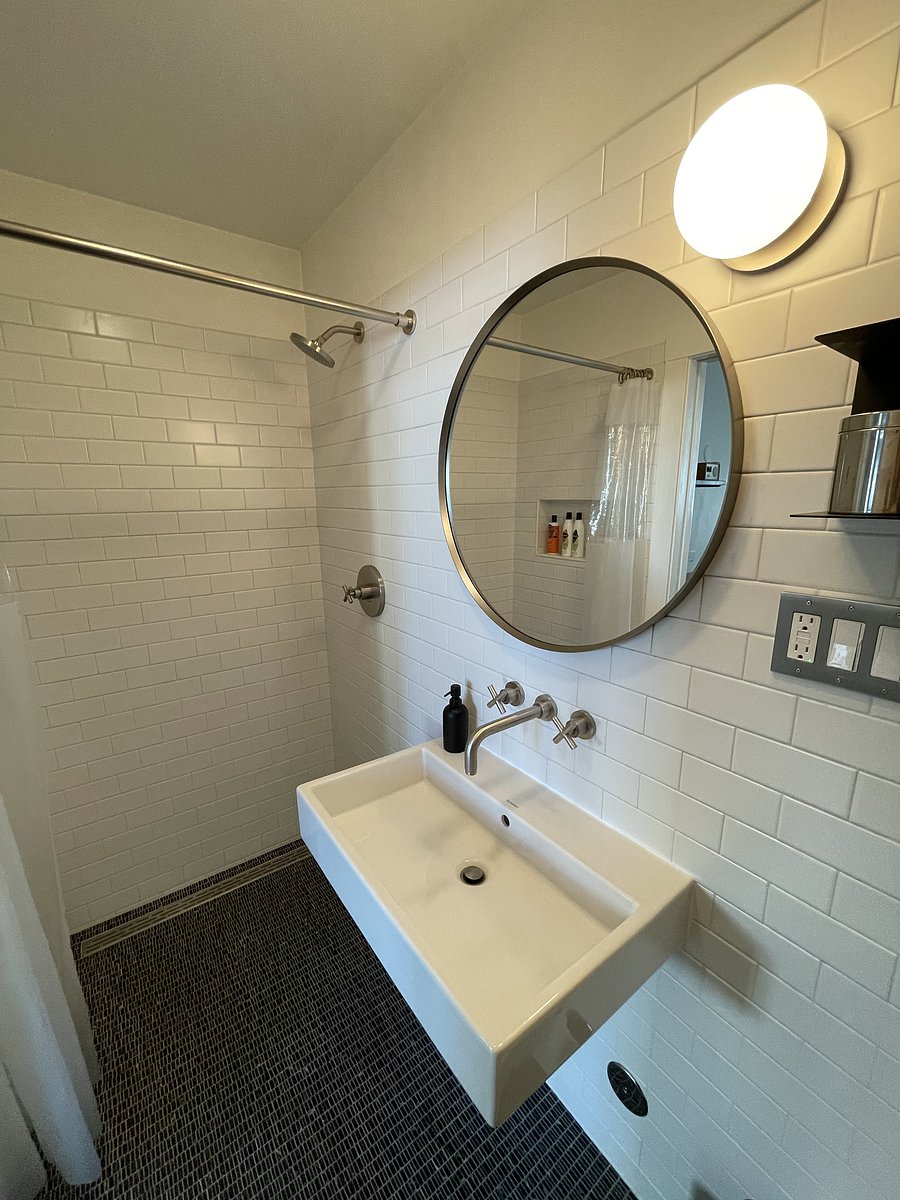Generous shower on one side of bathroom with curtain. Black marble tiled floor is sloped for draining.