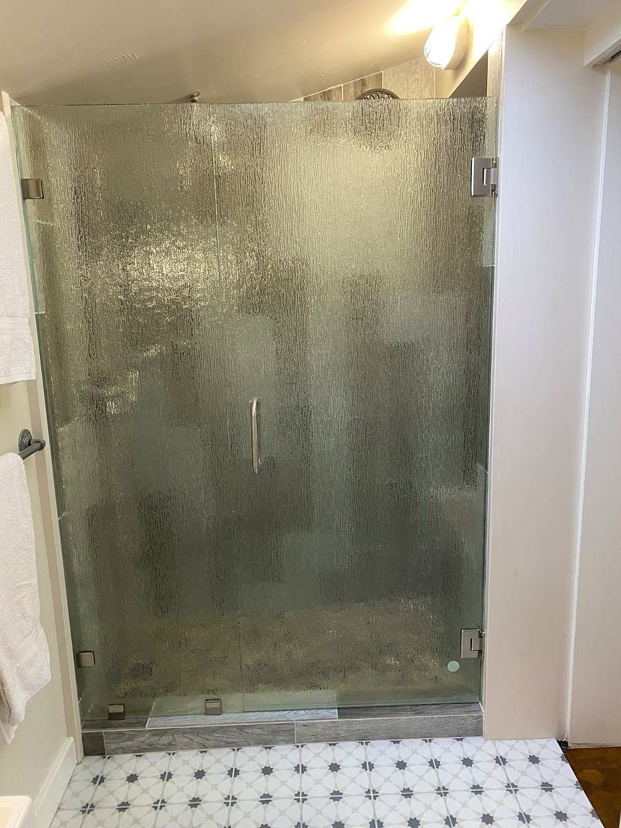A walk-in shower with a rain glass door. 