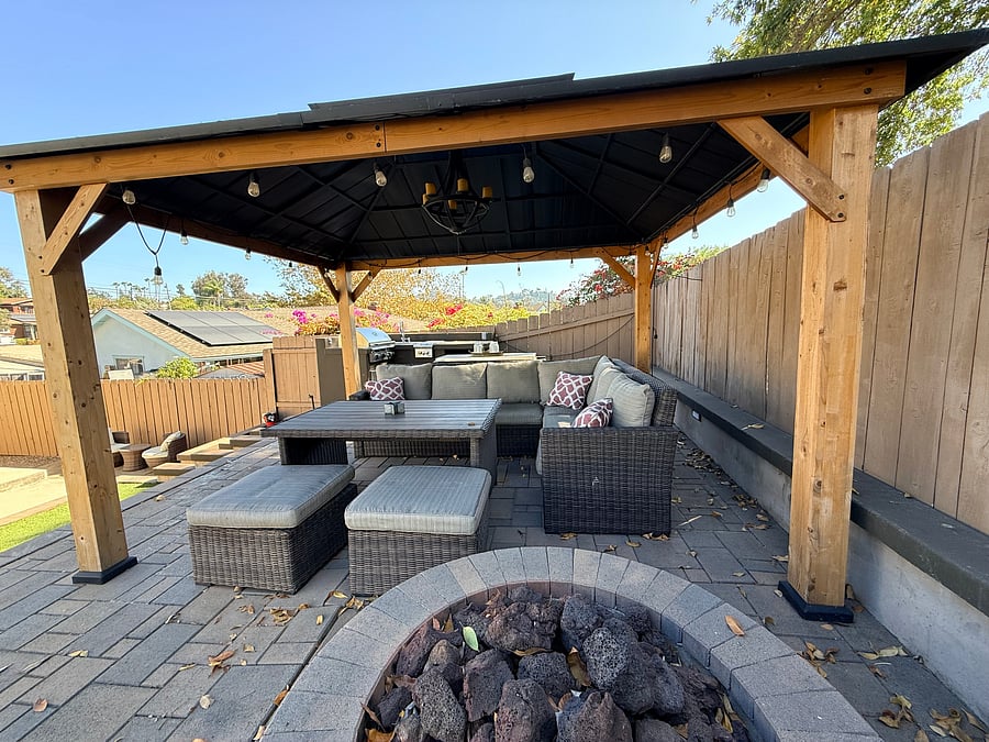 Closer view of the furnished patio, firepit, and gazebo. Kitchen and BBQ behind the couch.