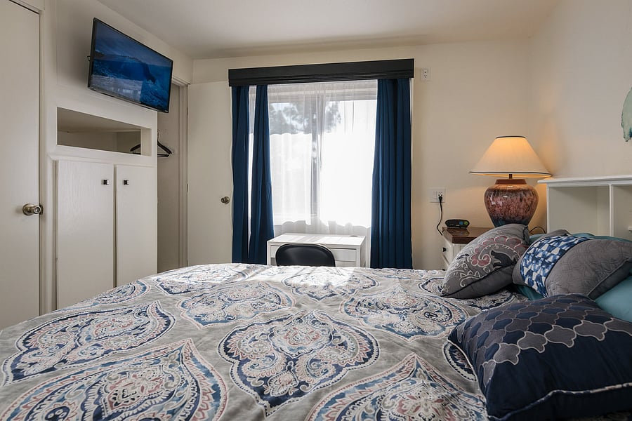 Left bedroom with paisley bedding, blue curtains, a wall-mounted TV, and bedside lighting