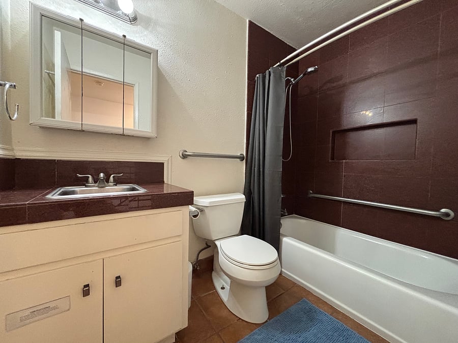 Full bathroom with a tub/shower combination, handheld showerhead, grab bars, and vanity storage