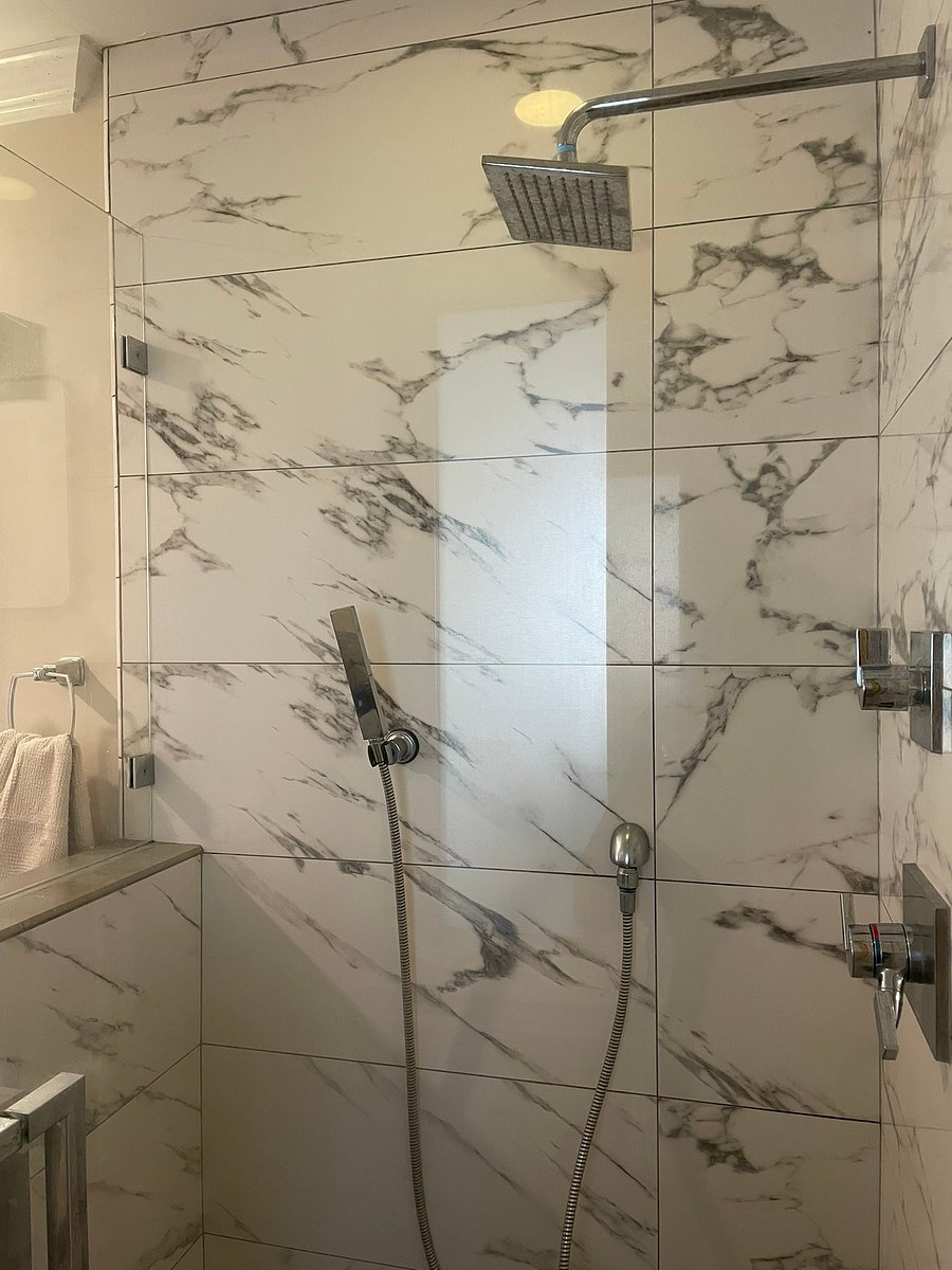 Walk-in shower featuring custom marble-style tile, rainfall showerhead, and a versatile handheld sprayer.