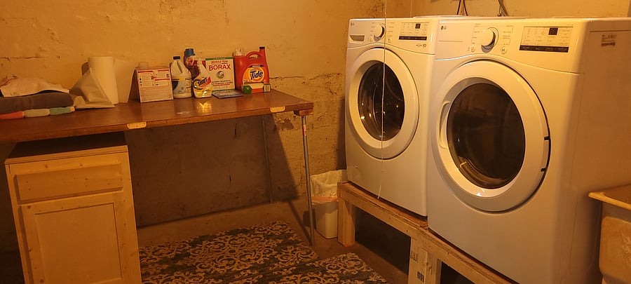New front load washer, drier, and folding table in bright basement.