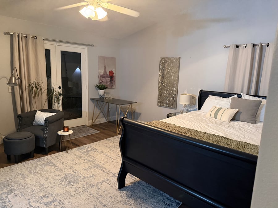 Full view of the sleeping and living portions of the master suite with black out curtains and ceiling fan.