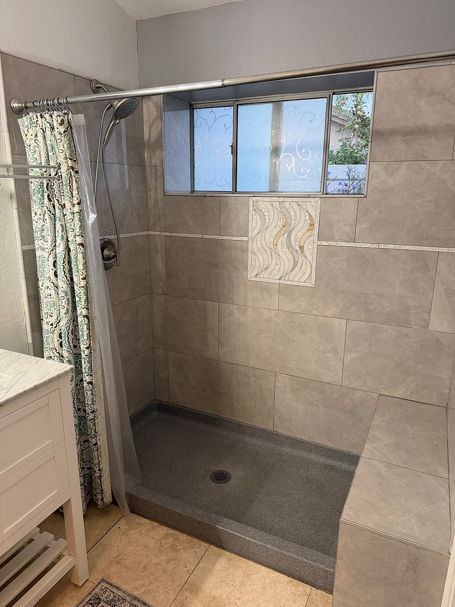 Open tiled shower with seat, shower-head, and flexible hose access.