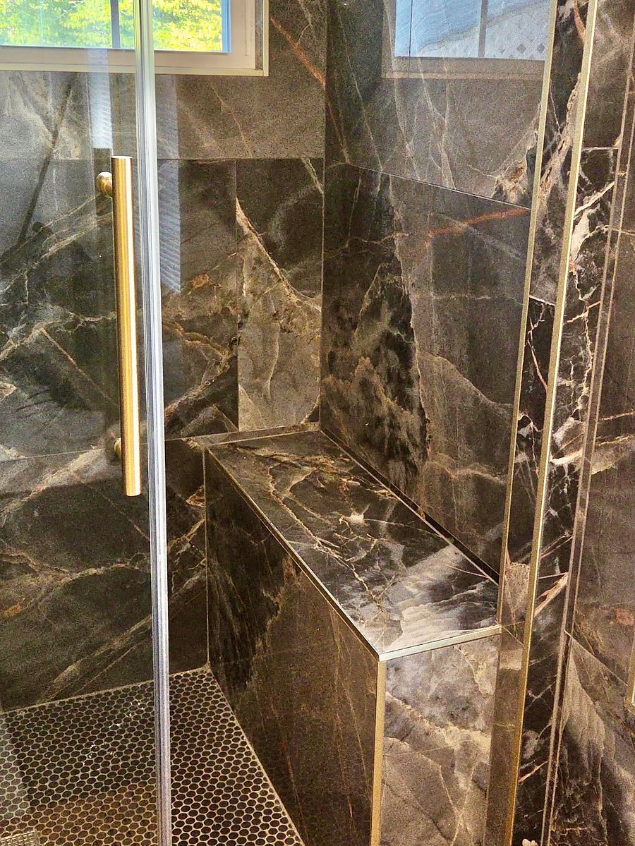 A spa-inspired bathroom with striking marble-look finishes, a glass-enclosed rainfall shower, and elegant gold accents-a beautiful place to refresh after a long day.
