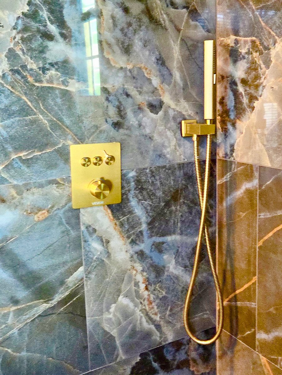 A spa-inspired bathroom with striking marble-look finishes, a glass-enclosed rainfall shower, and elegant gold accents-a beautiful place to refresh after a long day.