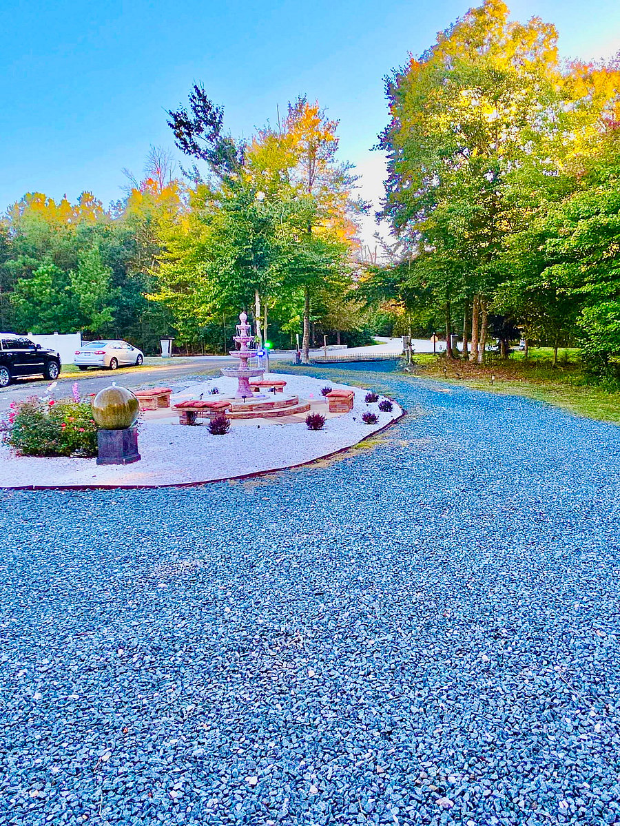 A spacious gravel drive curves around the landscaped fountain courtyard, offering convenient parking in a tranquil wooded setting. Open grounds, mature trees, and garden details make each arrival feel like a welcome return to your home away from home.