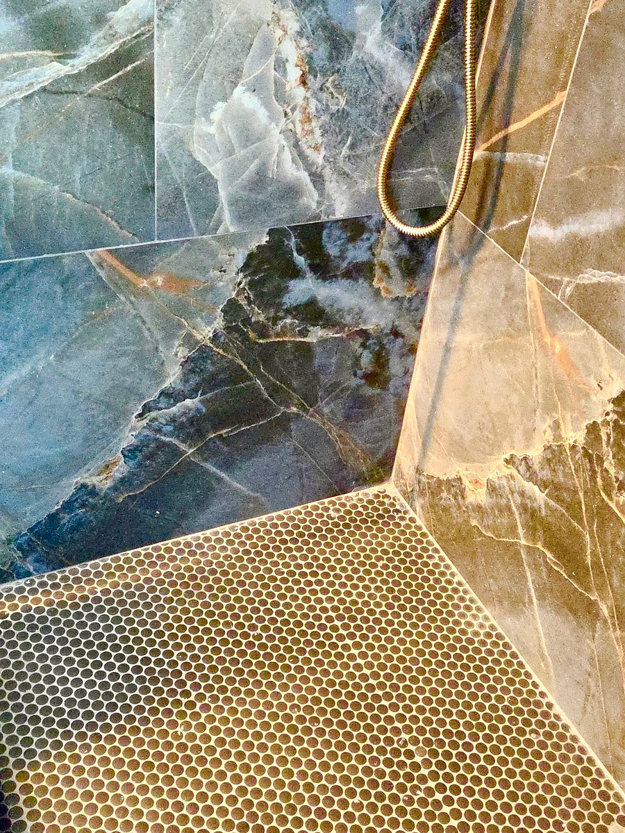 A spa-inspired bathroom with striking marble-look finishes, a glass-enclosed rainfall shower, and elegant gold accents-a beautiful place to refresh after a long day.