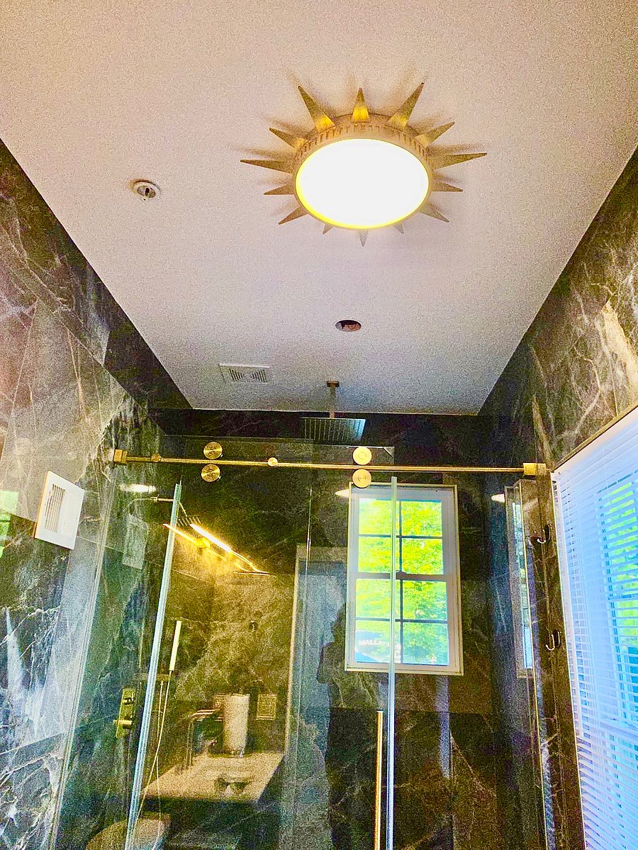 A spa-inspired bathroom with striking marble-look finishes, a glass-enclosed rainfall shower, and elegant gold accents-a beautiful place to refresh after a long day.
