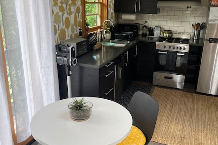 Full compact kitchen with stove, toaster, microwave, dishwasher, coffee maker. Small dining/work table and balcony doors open to provide more indoor/outdoor space and light.