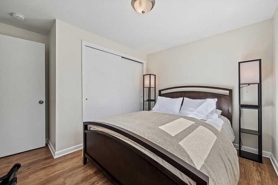 Master bedroom with queen bed and large closet with hangers, hanging shelves, and and ironing board with iron.
