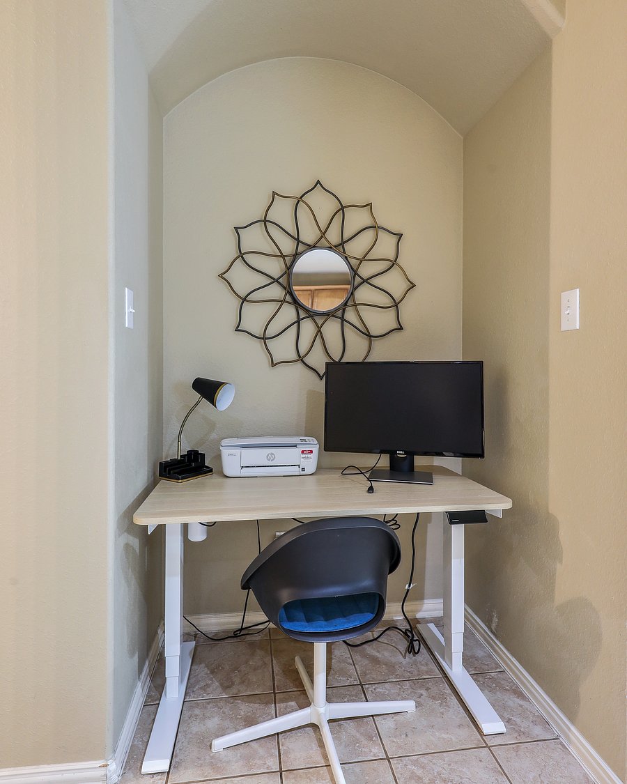 Dedicated office nook with sit-stand desk, chair, desk lamp and monitor.