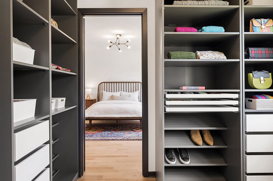 The primary bedroom's private ensuite walk-in closet includes built in dressers, cabinetry, and a mix of open and drawer storage for folded clothes, shoes, and adornments. Connects the primary bedroom with the private ensuite bathroom.
