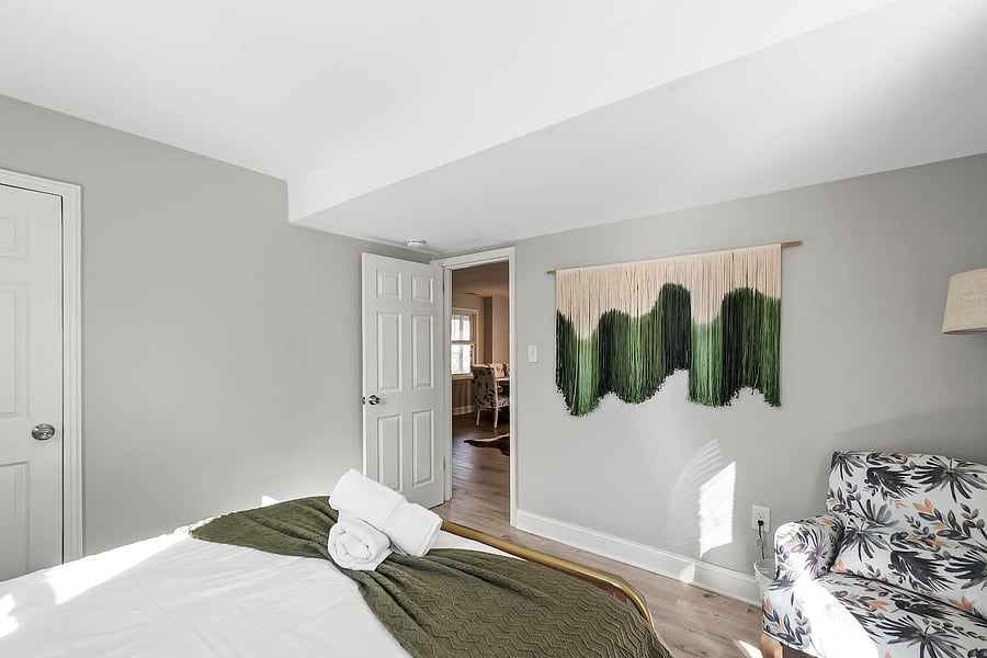 Queen bed with premium bedding, accent chairs & Ottoman, full-length mirrors, nightstands with charging ports, closet, and blackout curtains.