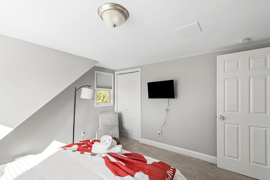 Spacious Queen bedroom with plush bedding, accent chairs & Ottoman, full-length mirror, nightstands, closet, blackout curtains, and smart TV.
