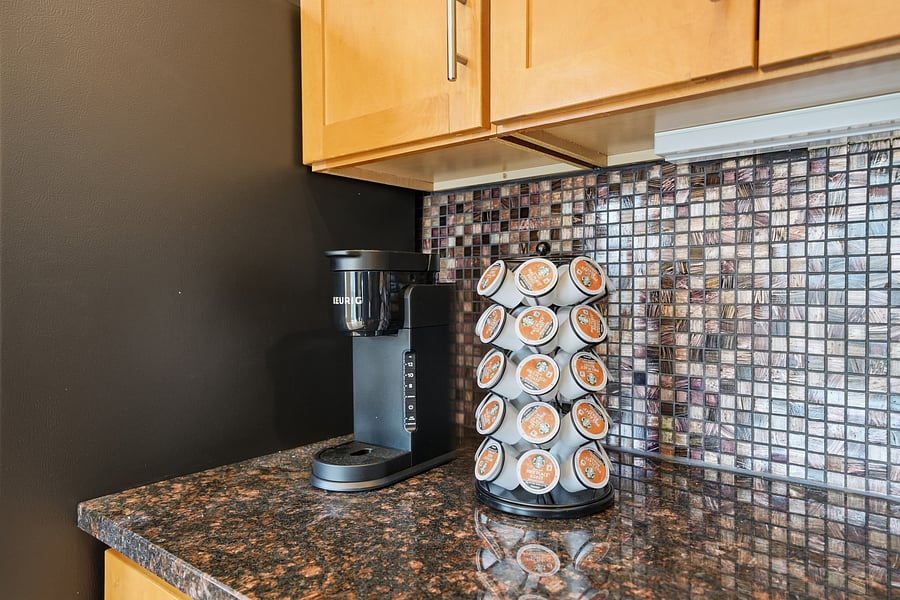 Kitchen: Fully stocked coffee station featuring a Keurig coffee maker and pod carousel set against custom tile backsplash and granite countertops. Start your morning right!