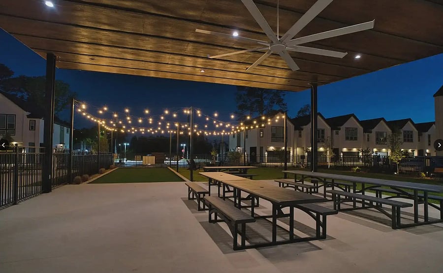 Covered pavilion with dining tables under string lights.